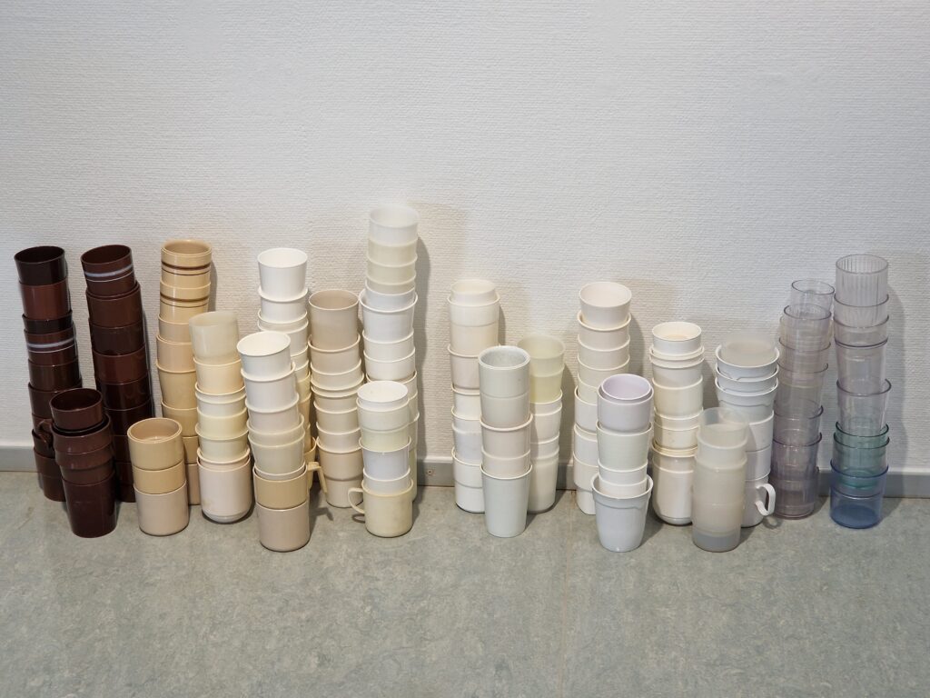 Muovisia mukeja pinottuna seinän viereen Tavaratalo-näyttelyssä.